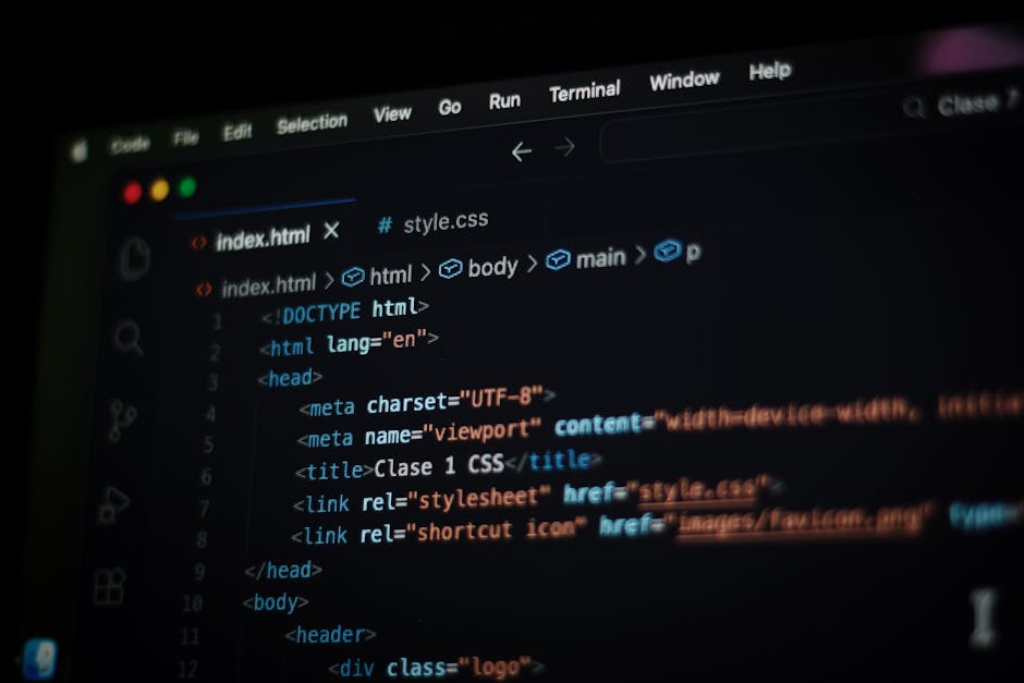 A close-up of a person's hands typing on a laptop keyboard placed on a dark, reflective surface. The laptop screen displays a dark-themed code editor with lines of multicoloured programming code, incl